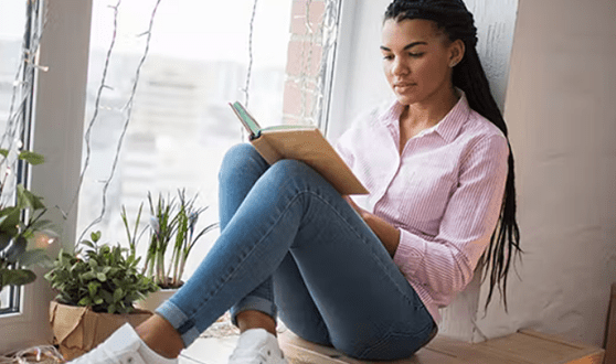 teen sitting in a window reading a book